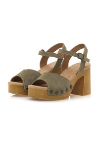 Las sandalias de plataforma de ante verde presentan un diseño de punta abierta, correas en los tobillos con hebilla, plantilla texturizada y un gran tacón cuadrado con tachuelas decorativas.