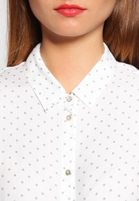 Vit skjorta med knappar som har gråa prickar, en klassisk krage och pärlemorknappar med en subtil lyster.