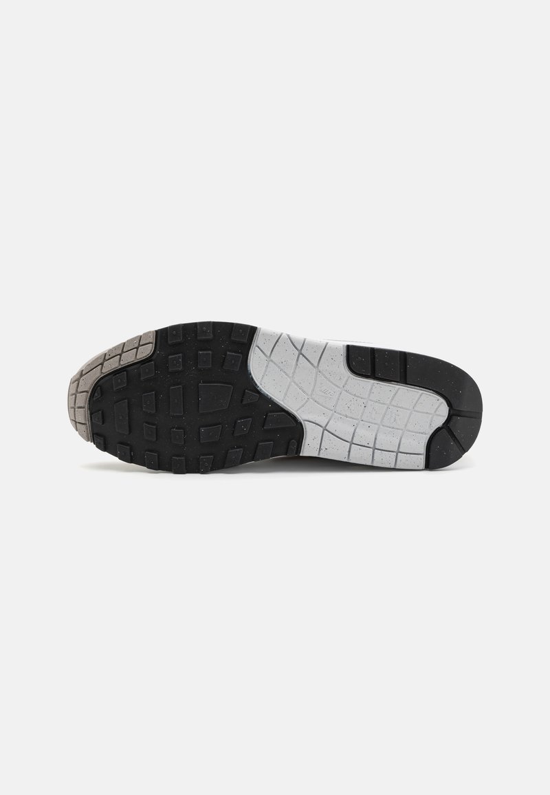 Suela de zapato con un diseño texturizado; goma negra en el talón, sección media salpicada de gris y blanco, y banda de rodadura con patrón para mayor agarre.