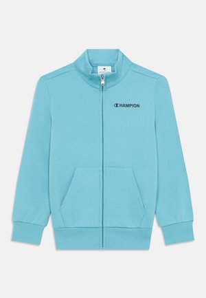 Sweatshirt de zíper azul claro com colarinho alto, dois bolsos frontais e um logótipo no peito esquerdo. Feito de material suave e texturizado.