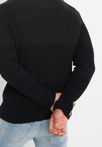 Suéter negro de punto, con un patrón texturizado de canalé, mangas largas y cuello redondo. La prenda tiene un diseño ajustado y un dobladillo recto.