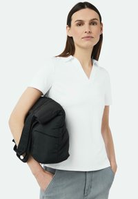 Weißes Polohemd mit V-Ausschnitt und kurzen Ärmeln, ergänzt durch einen schwarzen gepolsterten Rucksack mit Trägern und einer strukturierten Oberfläche.