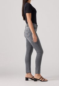 Grå denim skinny jeans med hög midja och subtilt fransad fåll; kombineras med en figurnära svart t-shirt och svarta klacksandaler.