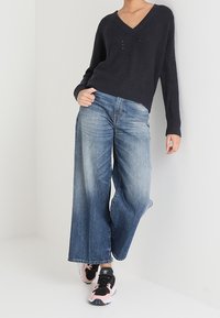 Pull en maille côtelée bleu marine avec un col en V, associé à un jean large bleu clair. Des baskets noires et roses complètent la tenue.