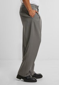 Pantalones de pierna ancha grises, confeccionados en un tejido suave con un corte relajado, que cuentan con bolsillos laterales y pasador de cinturón, combinados con zapatos negros.