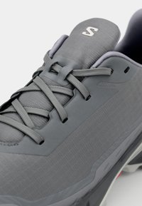 Botte de sport grise avec un dessus en tissu texturé, des accents synthétiques, des lacets plats et une semelle rembourrée présentant un logo discret sur la languette.