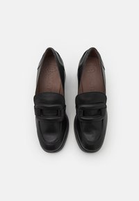 Mocasines de cuero negro con suela plana, punta redonda y una hebilla decorativa en la parte delantera, con una textura suave y un diseño minimalista.