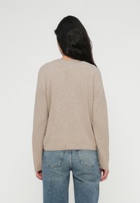 Μπεζ πουλόβερ πλεκτό με στρογγυλή λαιμόκοψη και μακριά μανίκια, με λεία υφή και χαλαρή εφαρμογή. Φορεμένο με μπλε τζιν ψηλόμεσο.