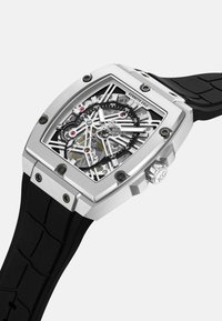 Szkieletowy zegarek na rękę z obudową ze stali nierdzewnej w kolorze srebrnym, czarnym paskiem z gumy i skomplikowanym cyferblatem, odsłaniającym wewnętrzne mechanizmy oraz czerwonymi akcentami.