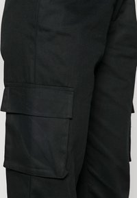 Czarne spodnie cargo wykonane z trwałego materiału, z bocznymi kieszeniami, gładką teksturą i prostym krojem nogawek.