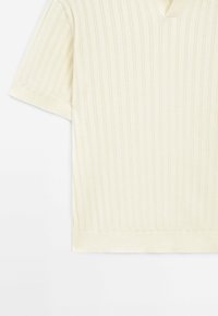 Pull court en tricot côtelé de couleur crème avec un col, montré de la moitié du torse jusqu'à la manche sur un fond blanc.