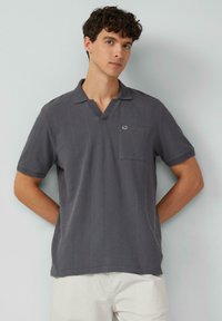 Szary krótki rękaw polo z dekoltem w serek, teksturowana tkanina, mała kieszonka na piersi i logo marki. Gładkie wykończenie i luźny krój.