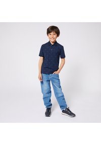 Navy polo shirt with subtle pattern, two buttons, and short sleeves, paired with light blue denim jeans and black athletic shoes.