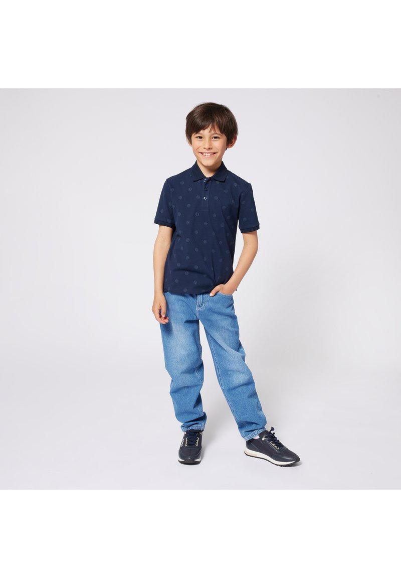 Navy polo shirt with subtle pattern, two buttons, and short sleeves, paired with light blue denim jeans and black athletic shoes.