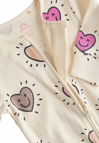 Ribbet creme baby onesie med pink og brun hjerte mønstre, med en fuld lynlås og en blød tekstur for komfort.