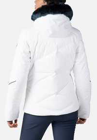 Bílá izolovaná bunda s límcem z umělé kožešiny v námořnické modři. Má přiléhavý střih s diamantovým prošíváním a bočním lemováním.