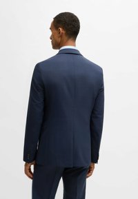Navy blue tailored suit jacket with a textured finish, single vent, and notched lapels. Features buttoned cuffs and a subtle check pattern.