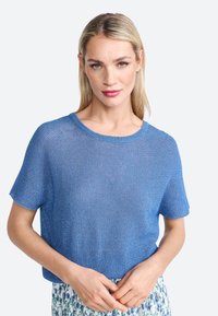 Top corto de punto azul con cuello redondo. Textura ligera y corte holgado. Combinado con una falda de estampado floral.
