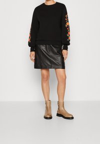 Černá mikina s květinovou výšivkou na rukávech, doplněná černou koženou sukní a béžovými kotníkovými botami se bočním zipem.