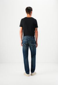 Camiseta negra de manga corta combinada con jeans de denim azul que presentan un diseño clásico de cinco bolsillos y sutiles acentos de costura en la parte posterior.