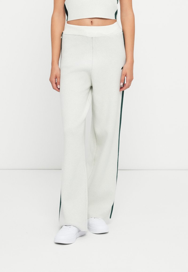 Pantaloni a gamba larga grigio chiaro, realizzati in tessuto morbido, con una vita bianca e strisce laterali verde scuro. Abbinati a sneakers bianche.