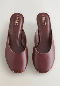 Scarpe slip-on in pelle color bordeaux con finitura liscia, caratterizzate da borchie dorate rotonde lungo il bordo e una soletta imbottita per il comfort.