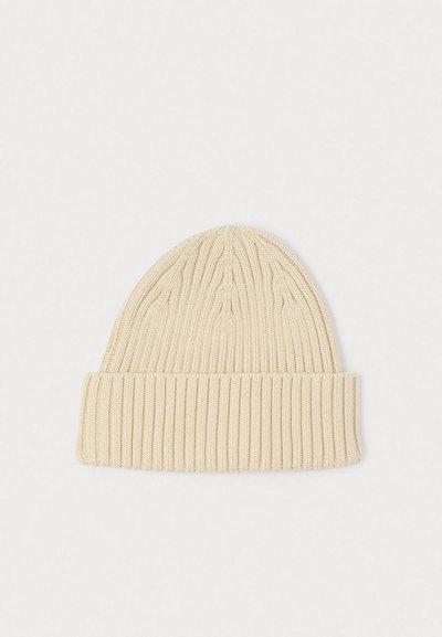 Knit beanie in light beige, featuring ribbed texture and a folded cuff. Soft material with a snug fit and rounded top design.