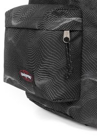 Svart tygväska med vågiga vita mönster, ficka med dragkedja och röd Eastpak-logotyp på sidan. Strukturerad yta, modern design.