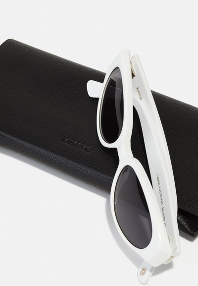 White sunglasses with dark lenses and a sleek, angular design, resting on a textured black leather case embossed with "kinéze."