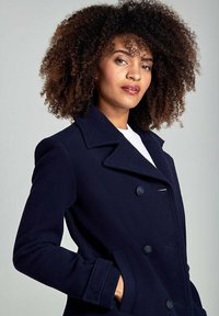 Cappotto in lana blu navy con design doppiopetto, ampie rever, due bottoni e tasche laterali. Tessuto liscio, vestibilità sartoriale.