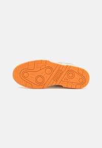 Suela de zapatilla PUMA con goma naranja texturizada, que presenta patrones circulares y triangulares, y un grabado del logo para mejorar el agarre y la durabilidad.