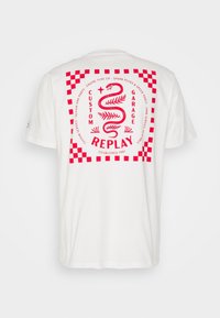 Bílý krátký rukáv tričko s červeným grafickým designem se hadem, šachovnicovým okrajem a textem "REPLAY" uspořádaným do kruhu.