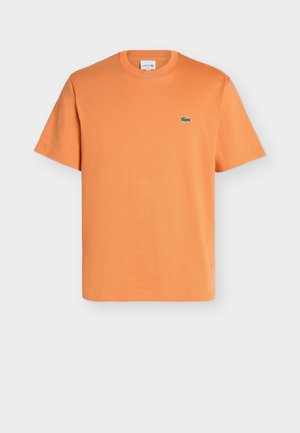 T-shirt orange à manches courtes avec col rond et petit logo crocodile vert Lacoste sur la poitrine gauche sur fond uni.