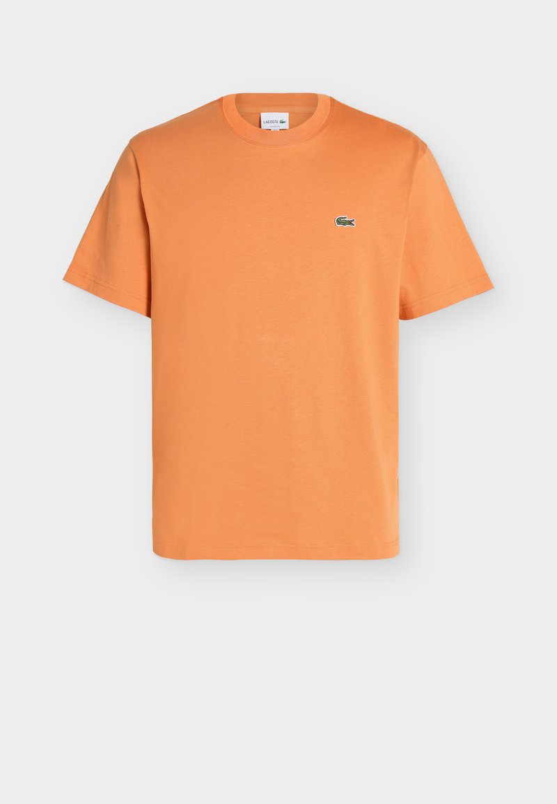 Oranje T-shirt met korte mouwen en een ronde hals, met een klein groen Lacoste-krokodillenlogo links op de borst tegen een effen achtergrond.