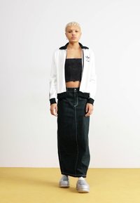 White zip-up jacket with black accents, black crop top, and long dark green ribbed skirt. Model wears chunky silver sneakers.