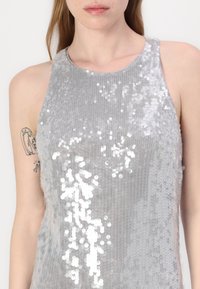Top prateado sem mangas com tecido texturizado, apresentando lantejoulas iridescentes dispostas de forma aleatória e um decote alto.