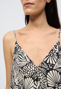 Μπλούζα με λεπτές τιράντες σε ασπρόμαυρο χρώμα, με σχέδιο σε σχήμα v-λαιμόκοψης, λουλουδένια μοτίβα και ελαφρύ ύφασμα με μαλακή υφή.