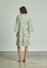 Vestito in pizzo caratterizzato da un motivo floreale verde menta, maniche a campana a tre quarti, vita aderente e gonna di lunghezza al ginocchio. Accentuato da dettagli a intreccio aperto.