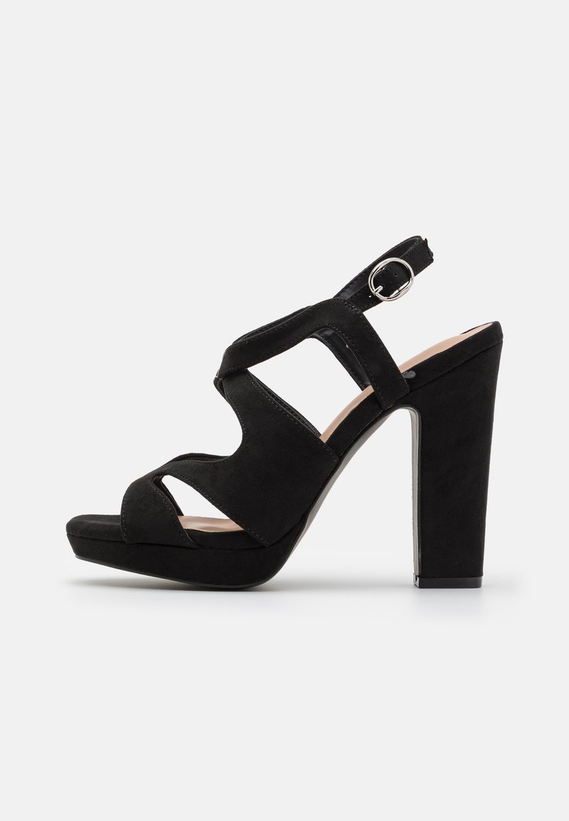 Sandale à talon haut en daim noir avec plateforme, bout ouvert, brides découpées et boucle ajustable à la cheville sur fond blanc.