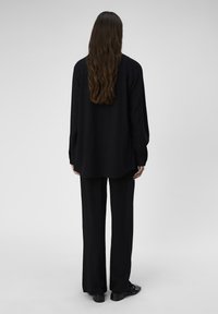 Sort langærmet skjorte kombineret med matchende vide bukser. Stoffet virker let og har en glat tekstur, designet til en afslappet pasform.