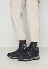 Svarta och marinblå vandringsskor i syntetmaterial, med metallöglor, en texturerad tygfinish och en gummisul med greppdetaljer.