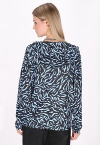 Svart huva jacka med ett blåt vågmönster, långa ärmar och avslappnad passform, tillverkad av lätt och slätt tyg.