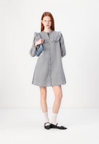 Abito grigio con colletto arricciato, chiusura con bottoni e motivo a pois. Maniche lunghe con polsini arricciati. Abbinato a ballerine nere e calze bianche.