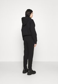 Sort cropped hættetrøje med hætte, der er parret med matchende sorte joggerbukser. Glat tekstur; modellen har chunky sorte støvler på.