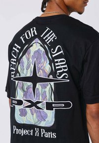 Camiseta de algodón negra con un gran gráfico en la parte posterior que presenta diseños florales, un texto que dice "Alcanza las Estrellas" y la marca "PXP."