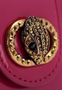 Materiale in vernice fucsia brillante con una fibbia decorativa oro e nera caratterizzata da un design texture e dettagli luccicanti.