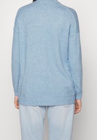 Pull bleu clair tricoté avec un col montant, un ourlet côtelé et des épaules tombantes. Texture douce et coupe décontractée, associé à un pantalon en denim clair.