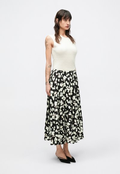 Biely bezrukávový top v kombinácii s dlhou čiernou plisovanou sukňou s kvetinovým vzorom v bielej a svetloružovej farbe. Čierne topánky so špičatou špičkou.