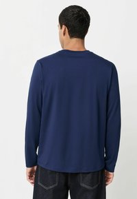 Cămașă cu mânecă lungă de culoare bleumarin, dintr-un material neted și elastic, cu decolteu rotund, având un tiv drept și detalii minime.