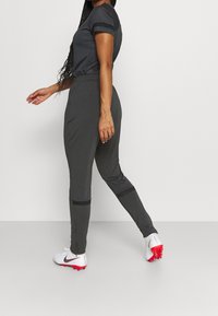 Gråt atletisk sæt med en tætsiddende kortærmet top og tilspidsede bukser, med sorte accentstriber og hvide fodboldstøvler med røde såler.